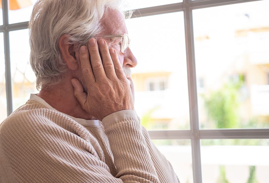 elderly man staring out of the window looking worried.